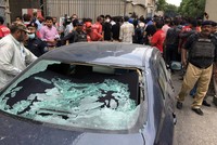 Đám đông tụ tập gần một chiếc xe bị bắn vỡ cửa kính tại lối vào sở giao dịch chứng khoán ở Karachi, Pakistan hôm nay. Ảnh: Reuters.