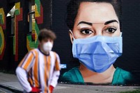 Một người đàn ông đi qua một bức vẽ mô tả một y tá đeo khẩu trang ở London, Anh. (Ảnh: Reuters).