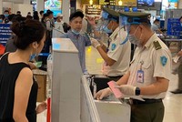 Nhân viên an ninh hàng không được trang bị đầy đủ găng tay, khẩu trang, tấm chắn giọt bắn trong khi đo thân nhiệt cho hành khách.