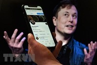 Tài khoản Twitter của tỷ phú Elon Musk trên màn hình điện thoại và ảnh chụp ông Musk (phía sau) tại một sự kiện ở Washington, DC, Mỹ ngày 14/4. (Ảnh: AFP/TTXVN)