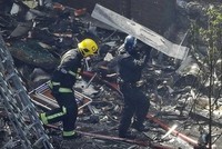 Cảnh sát che chắn cho lính cứu hỏa trong lúc bước qua những mảnh vỡ la liệt tại sân chung cư Grenfell. Ảnh:AP