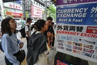 Người dân đứng bên ngoài quầy đổi tiền để xem tỷ giá đồng yên so với ngoại tệ, dọc con phố ở trung tâm Tokyo vào ngày 29/4/2024. Ảnh: AFP