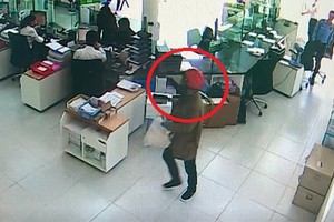 Tên cướp (khoanh tròn đỏ) cầm bao tải trắng tiến thẳng vào quầy gom tiền. Ảnh: Cắt từ camera.