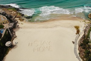 Lời kêu gọi ở nhà để tuân thủ quy định giãn cách xã hội được viết trên một bãi biển ở Sydney. Nguồn Getty.
