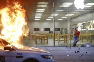 Một người chạy khỏi Apple Store tại Philadelphia trong khi một chiếc xe cảnh sát đỗ phía trước cửa hàng bị đốt cháy, ngày 30/5/2020. (Nguồn: AP).