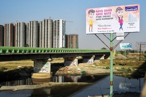 Bảng quảng cáo của một nhà môi giới bất động sản với hình ảnh một nhân vật cầm tờ tiền 2.000 rupee mới cùng slogan “Nhà mới, tiền mới”, gần khu vực đang xây dựng các tòa chung cư tại Uttar Pradesh

