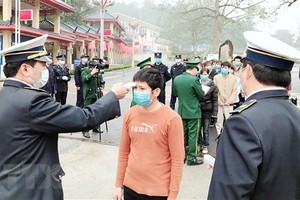 Cán bộ Trung tâm Kiểm dịch Y tế Quốc tế Cửa khẩu Quốc tế Hữu Nghị tiến hành đo thân nhiệt các công dân bị trao trả ngay tại biên giới trước khi làm thủ tục nhập cảnh vào Việt Nam. (Ảnh: Thái Thuần/TTXVN).