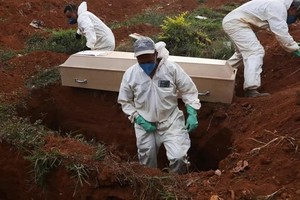 Những phu đào mộ mặc đồ bảo hộ chuẩn bị chôn cất quan tài một nạn nhân Covid-19 trong tang lễ không có người thân ở Sao Paolo, Brazil hôm 22/5. Ảnh: AFP.