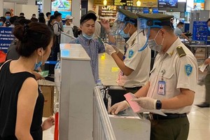 Nhân viên an ninh hàng không được trang bị đầy đủ găng tay, khẩu trang, tấm chắn giọt bắn trong khi đo thân nhiệt cho hành khách.