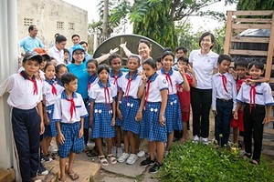 Chị Nguyễn Hồng Hạnh, cán bộ Nước sạch, Vệ sinh môi trường - UNICEF Việt Nam (áo xanh, bên trái) và cán bộ Masterise Group chia sẻ niềm vui với các em học sinh trường Tiểu học Long Phú C khi đón thiết bị nhà vệ sinh không phát thải. Ảnh: UNICEF Việt Nam/Trương Việt Hùng.