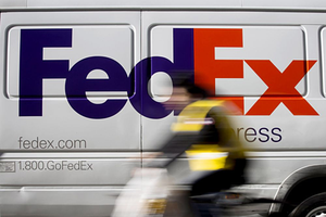 Một chiếc xe đạp lướt quaxe tải giao hàng FedEx đang đỗ tại khuMidtown,New York.Ảnh: Bloomberg.