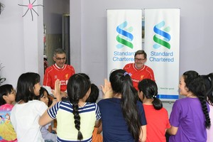 Ông Andy Halford, Giám đốc Tài chính Toàn cầu, Ngân hàng Standard Chartered (áo đỏ bên phải) và ông Nirukt Sapru, Tổng Giám đốc Ngân hàng Standard Chartered Việt Nam và nhóm 5 nước Đông Nam Á và Nam Á (áo đỏ bên trái), chia sẻ kiến thức tài chính với các bé gái ở Mái ấm Bà Chiểu.