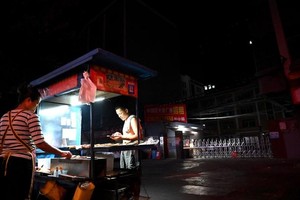 Một người bán đồ ăn trước lối vào một khu công nghiệp ở thành phố Đông Quan, tỉnh Quảng Đông, Trung Quốc - nơi bị ảnh hưởng bởi thiếu điện. Ảnh: AFP