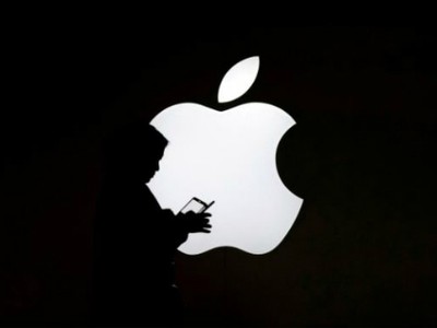 Một phụ nữ nhìn vào màn hình điện thoại di động của mình trước logo bên ngoài Apple Store ở Thượng Hải, Trung Quốc. Ảnh: Reuters.