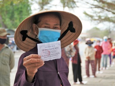 Bà Trần Thị Đảnh, 65 tuổi, cầm phiếu, đứng đầu hàng chuẩn bị vào bấm máy nhận gạo trước trụ sở phường Mũi Né.