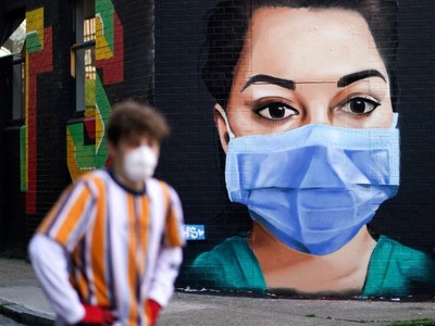 Một người đàn ông đi qua một bức vẽ mô tả một y tá đeo khẩu trang ở London, Anh. (Ảnh: Reuters).