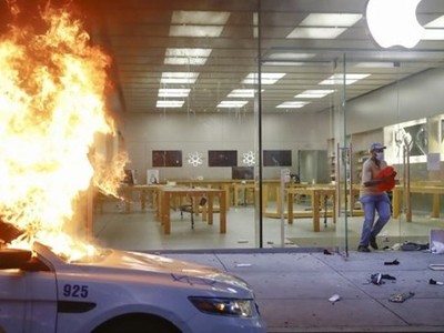 Một người chạy khỏi Apple Store tại Philadelphia trong khi một chiếc xe cảnh sát đỗ phía trước cửa hàng bị đốt cháy, ngày 30/5/2020. (Nguồn: AP).