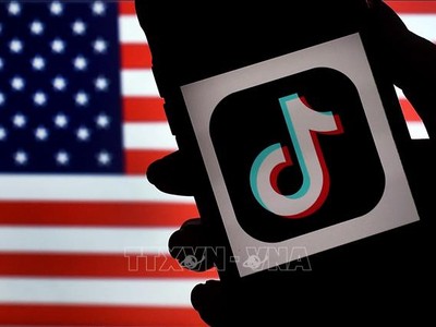 Biểu tượng ứng dụng TikTok trên màn hình điện thoại và quốc kỳ Mỹ (phía sau). Ảnh: AFP/TTXVN
