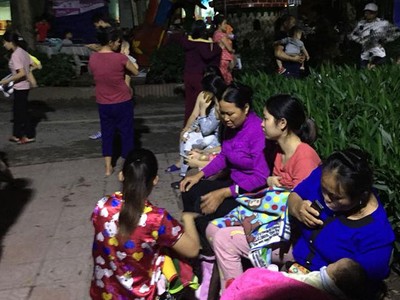 Người nhà bế theo bệnh nhi ngồi chờ dưới sân tòa nhà. Ảnh: Hương Giang.