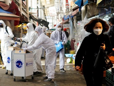 Một người phụ nữ Hàn Quốc đeo khẩu trang khi các nhân viên của công ty diệt khuẩn làm việc tại khu chợ truyền thống tại Seoul hôm 26/2. Ảnh: Reuters.