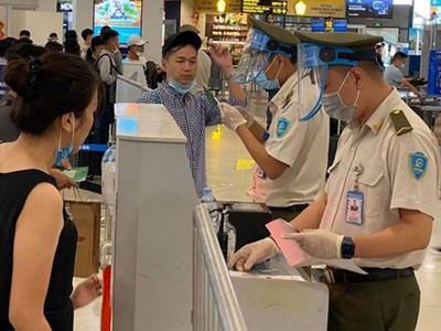 Nhân viên an ninh hàng không được trang bị đầy đủ găng tay, khẩu trang, tấm chắn giọt bắn trong khi đo thân nhiệt cho hành khách.
