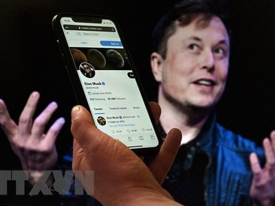 Tài khoản Twitter của tỷ phú Elon Musk trên màn hình điện thoại và ảnh chụp ông Musk (phía sau) tại một sự kiện ở Washington, DC, Mỹ ngày 14/4/2022. (Ảnh: AFP/TTXVN).