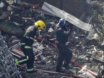 Cảnh sát che chắn cho lính cứu hỏa trong lúc bước qua những mảnh vỡ la liệt tại sân chung cư Grenfell. Ảnh:AP