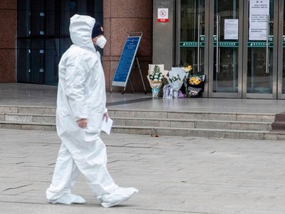 Một nhân viên y tế đi qua nơi đặt hoa tưởng niệm bác sĩ Lý Văn Lượng ở Vũ Hán ngày 7/2. Ảnh: AFP.