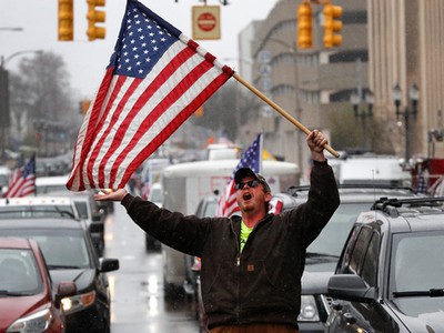 Người đàn ông cầm cờ Mỹ biểu tình phản đối phong tỏa vì Covid-19 tại thành phố Lansing, bang Michigan, hồi tháng 4. Ảnh: AP.