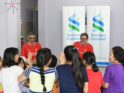 Ông Andy Halford, Giám đốc Tài chính Toàn cầu, Ngân hàng Standard Chartered (áo đỏ bên phải) và ông Nirukt Sapru, Tổng Giám đốc Ngân hàng Standard Chartered Việt Nam và nhóm 5 nước Đông Nam Á và Nam Á (áo đỏ bên trái), chia sẻ kiến thức tài chính với các bé gái ở Mái ấm Bà Chiểu.