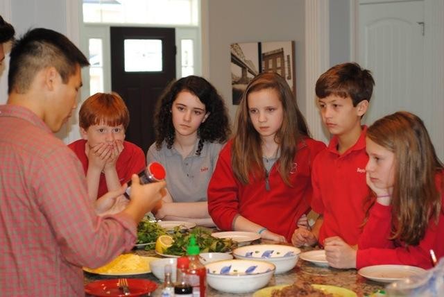 Đỗ Bảo Dương, con trai của ông Đỗ Cao Bảo (áo kẻ) đang chế biến các món ăn Việt Nam trước sự chứng kiến của các bạn khi học phổ thông tại Baylor Highschool