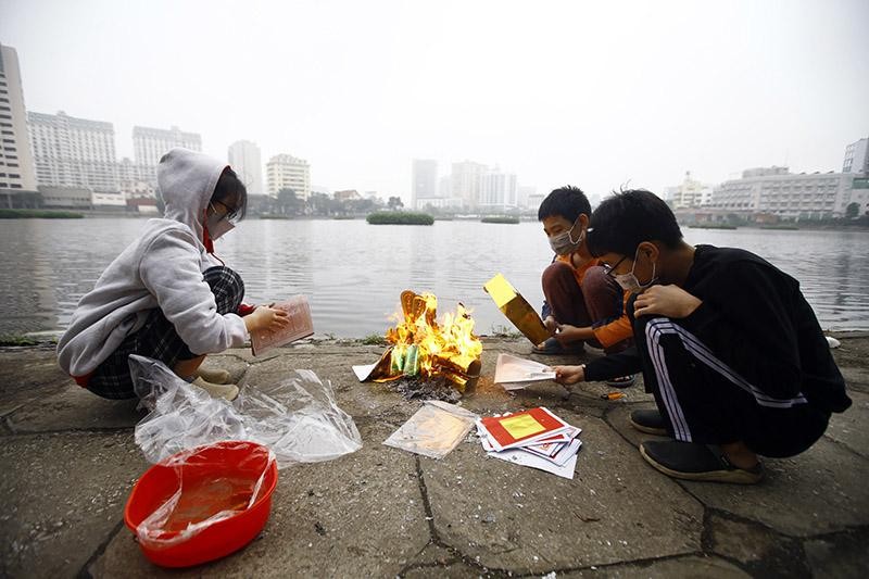 Một nhóm trẻ em trong một gia đình thay bố mẹ làm việc đốt vàng mã trước khi thả cá