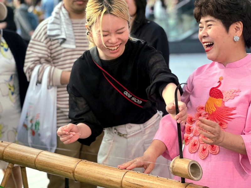 Chị Yuka (Nhật Bản) thích thú chơi thử đàn bầu với NSƯT Bùi Lệ Chi.