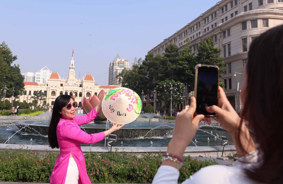 Một phụ nữ mặc áo dài chụp ảnh lưu niệm với nón lá trước quảng trường trung tâm thành phố.
