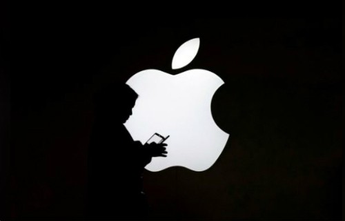 Một phụ nữ nhìn vào màn hình điện thoại di động của mình trước logo bên ngoài Apple Store ở Thượng Hải, Trung Quốc. Ảnh: Reuters.